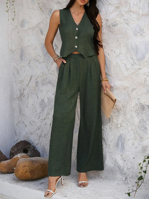 Woman wearing a green outfit with a vest and wide-leg pants against a textured wall.