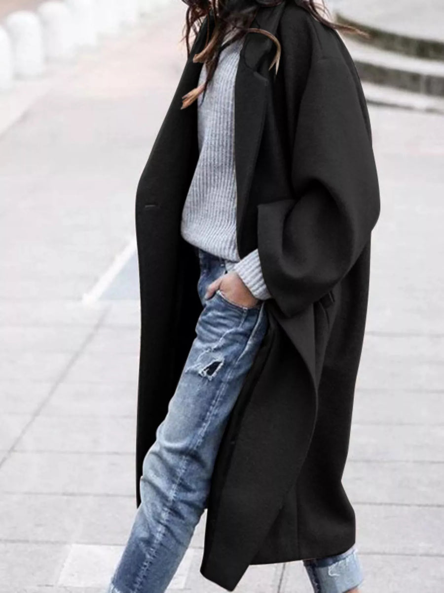 Person wearing a black coat over a light gray sweater and blue jeans on a blurred background