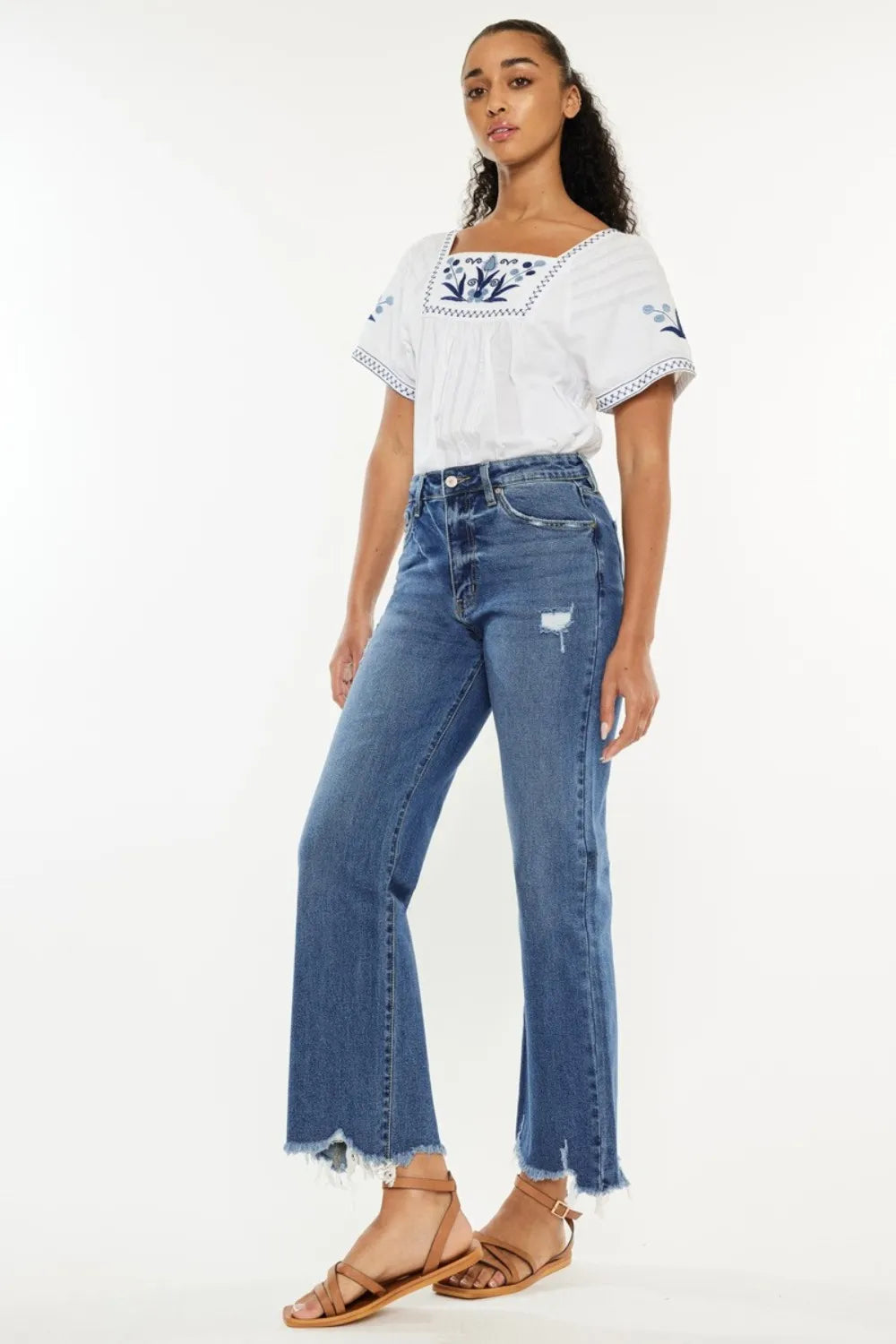 Woman wearing a white top with blue embroidery and blue jeans on a white background