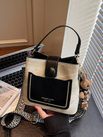 Beige and black handbag held by a person with a laptop and book in the background