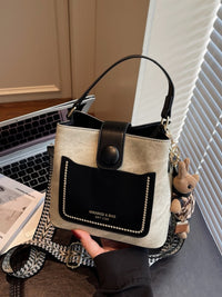 Beige and black handbag held by a person with a laptop and book in the background