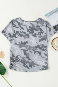 Camouflage-patterned shirt on a white surface with a magazine and cup in the background