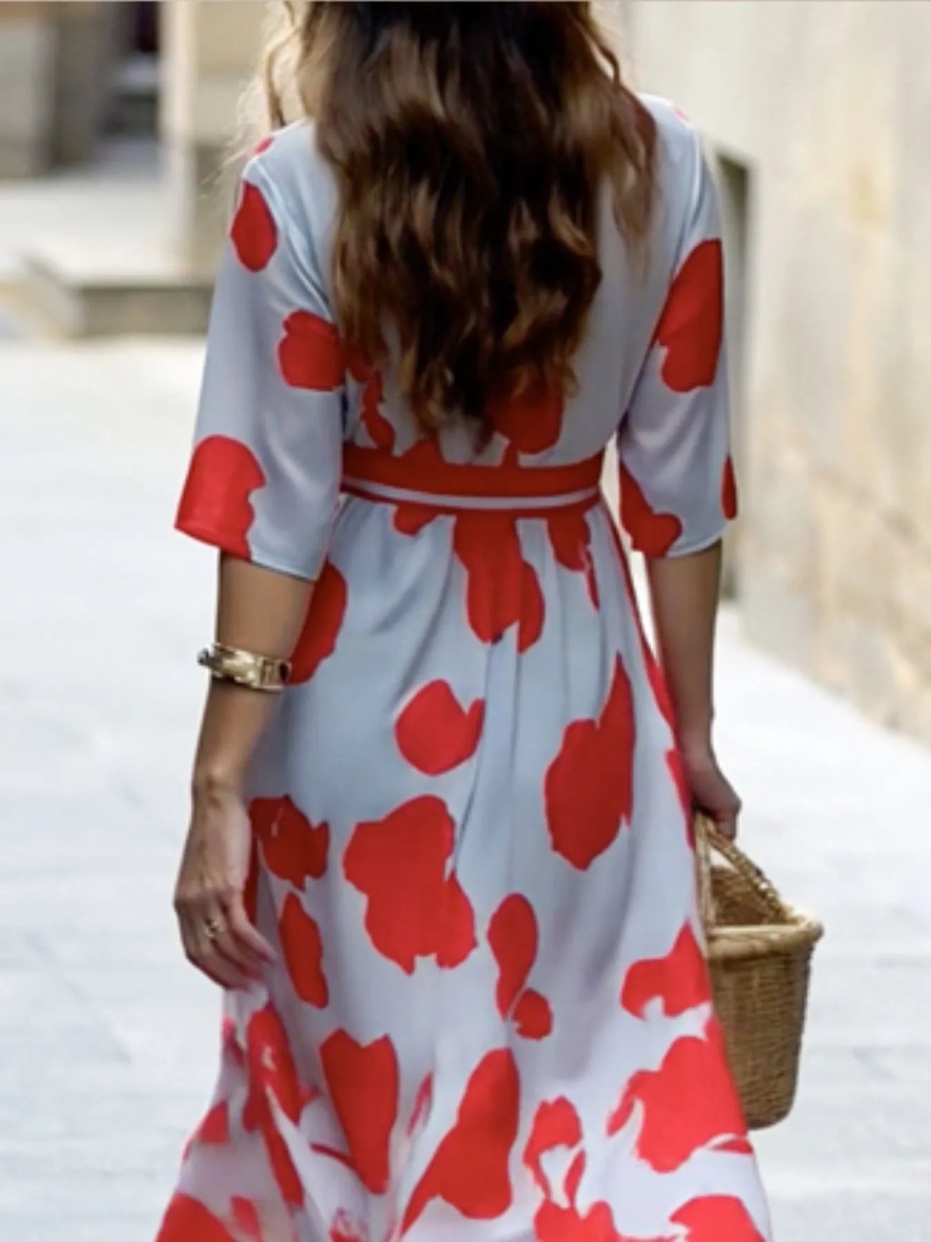 Woman wearing a red and white floral dress walking outdoors.