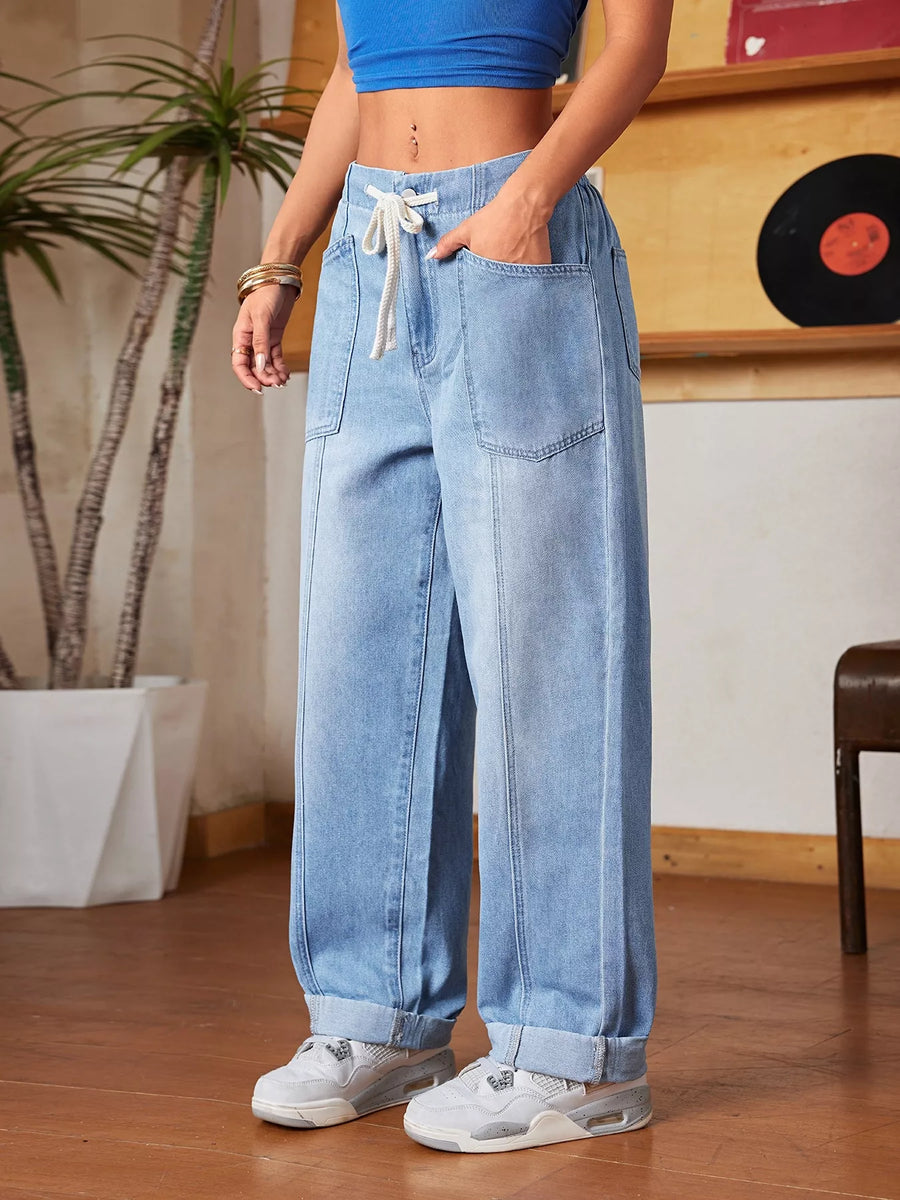 Person wearing blue jeans and a blue top in an indoor setting with a plant and record player in the background.