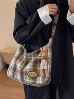 Plaid handbag with a teddy bear charm held by a person wearing a dark coat.