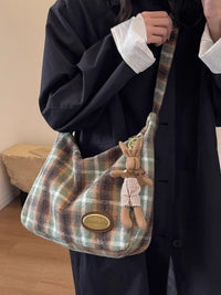 Plaid handbag with a teddy bear charm held by a person wearing a dark coat.