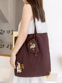 Brown tote bag with character design held by a person in a white dress.
