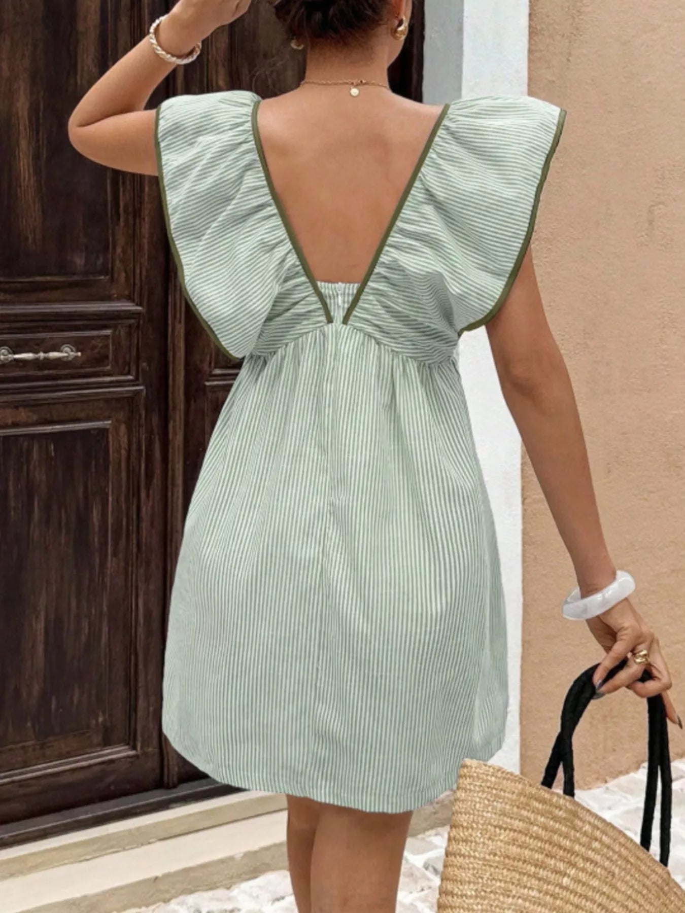 Woman wearing a green dress with a backless design, standing in front of a wooden door.