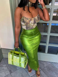 Woman wearing a camouflage top and green skirt, holding a green bag.
