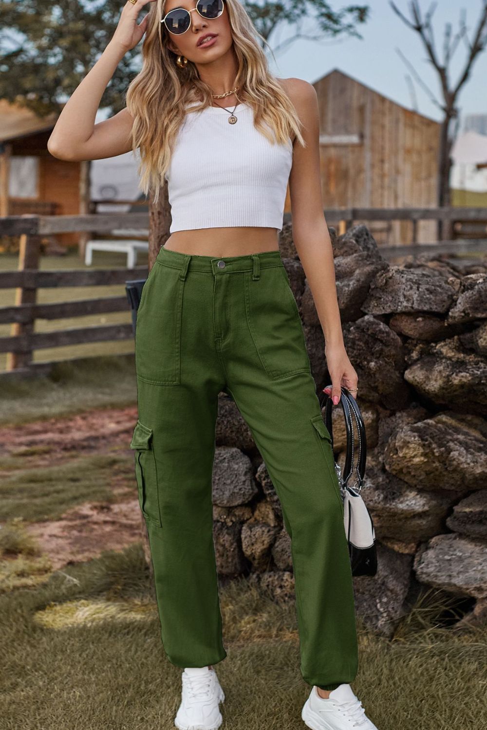 Woman wearing a white crop top and green cargo pants standing in front of a stone wall.
