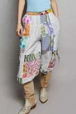 Person wearing colorful patchwork pants and beige boots on a plain background