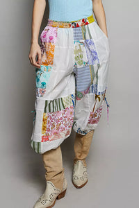 Person wearing colorful patchwork pants and beige boots on a plain background