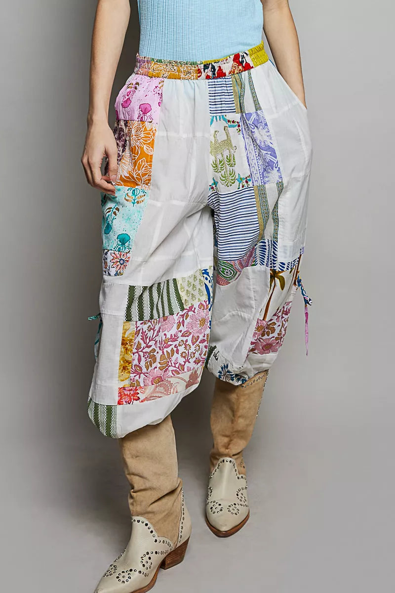 Person wearing colorful patchwork pants and beige boots on a plain background