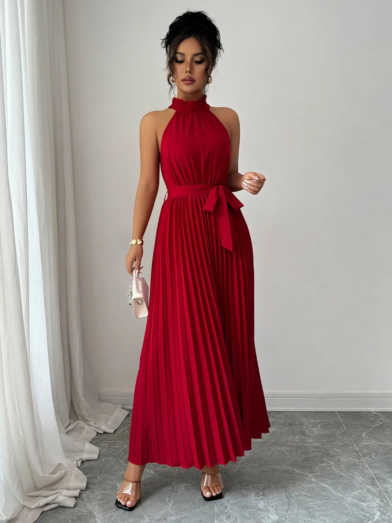 Woman wearing a red halter neck dress with a belt in a minimalistic setting.