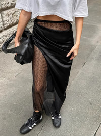 Person wearing a black sheer skirt over a white top on a sidewalk.