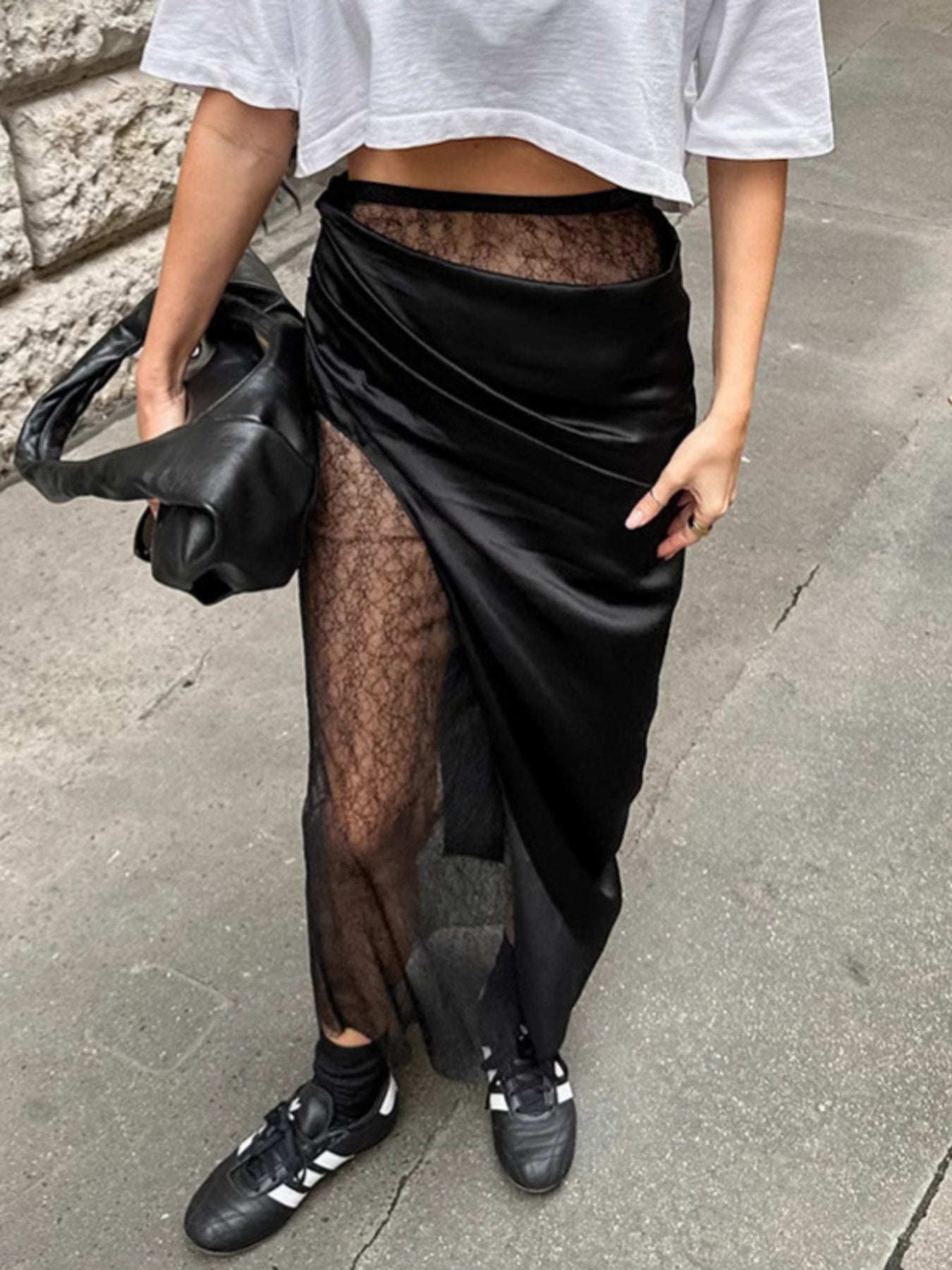Person wearing a black sheer skirt over a white top on a sidewalk.