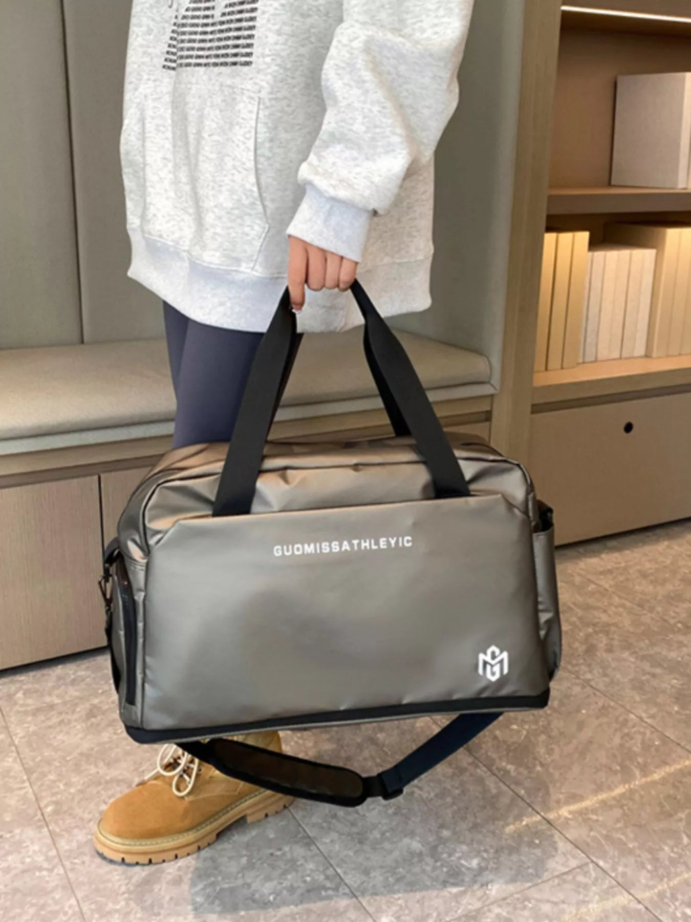 Person holding a gray duffel bag with black straps in an indoor setting