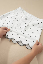 White fabric with black polka dots held by hands on a beige background