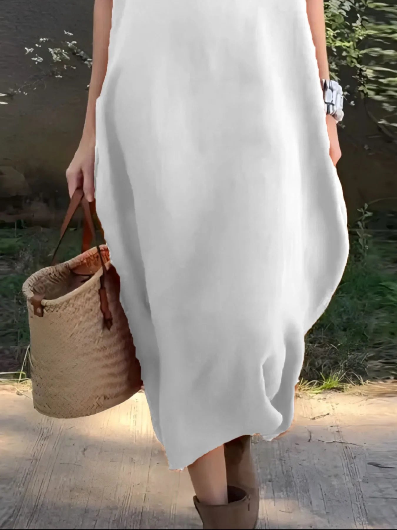 Person wearing a white dress holding a woven bag outdoors.