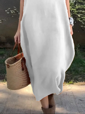 Person wearing a white dress holding a woven bag outdoors.