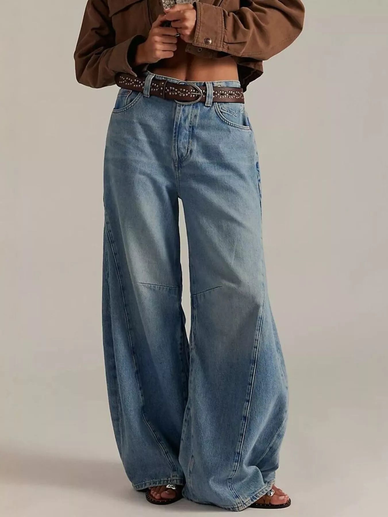 Person wearing wide-leg jeans and a brown jacket on a plain background