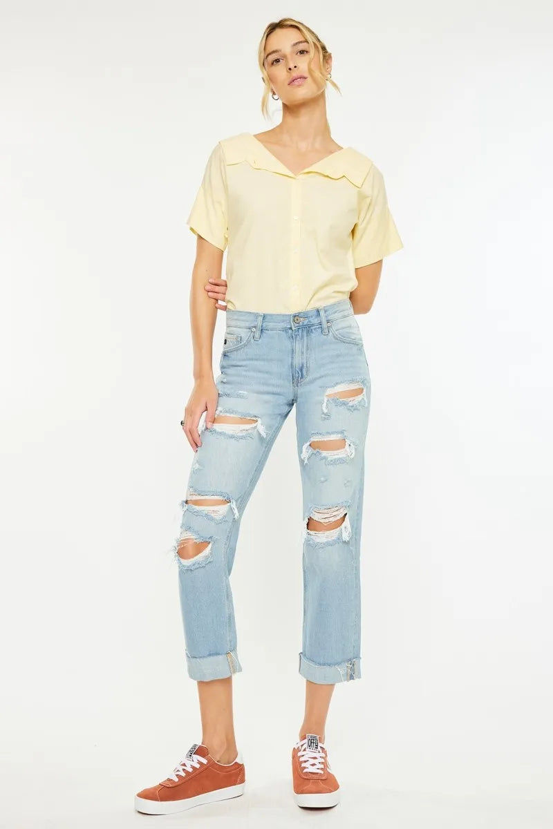 Woman wearing a yellow top and light blue ripped jeans on a white background