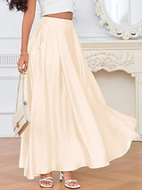 Woman wearing a long beige skirt with a white top and sandals, holding a small handbag.