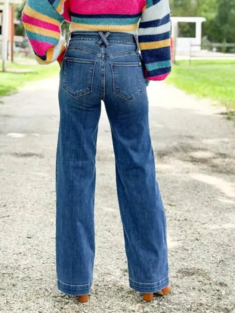 Person wearing blue jeans and a colorful striped sweater outdoors.