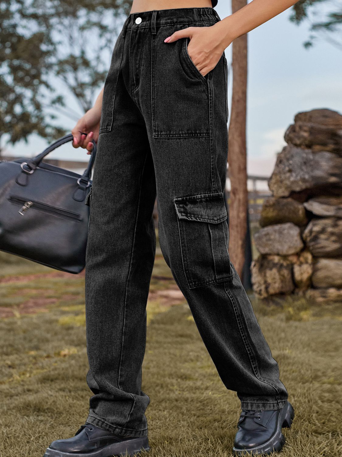 Person wearing black cargo pants holding a black bag outdoors.