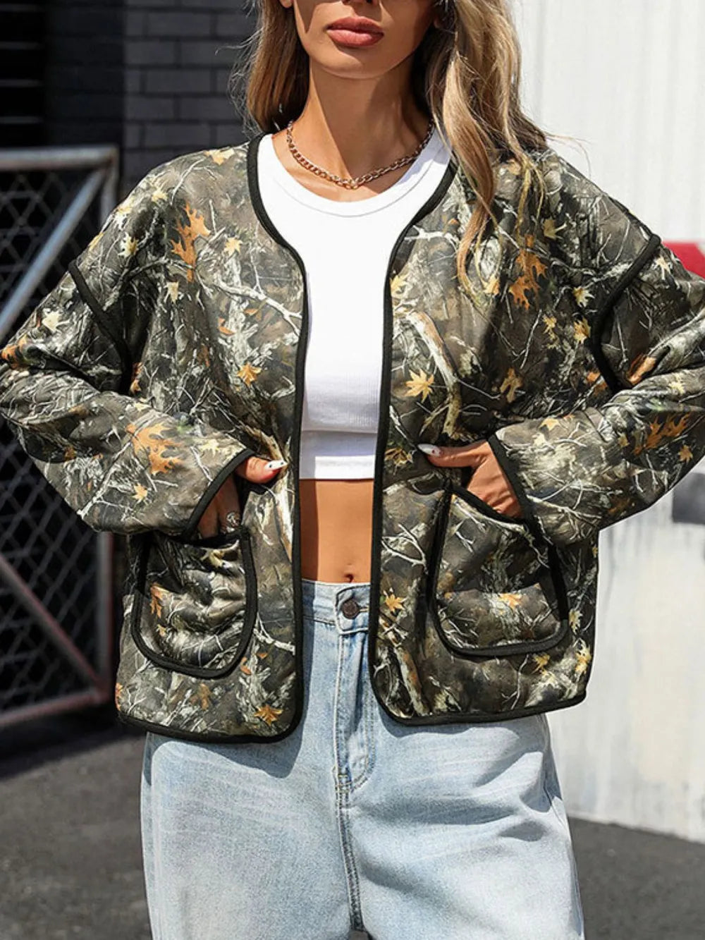 Person wearing a camouflage jacket with a white top and light blue jeans outdoors.
