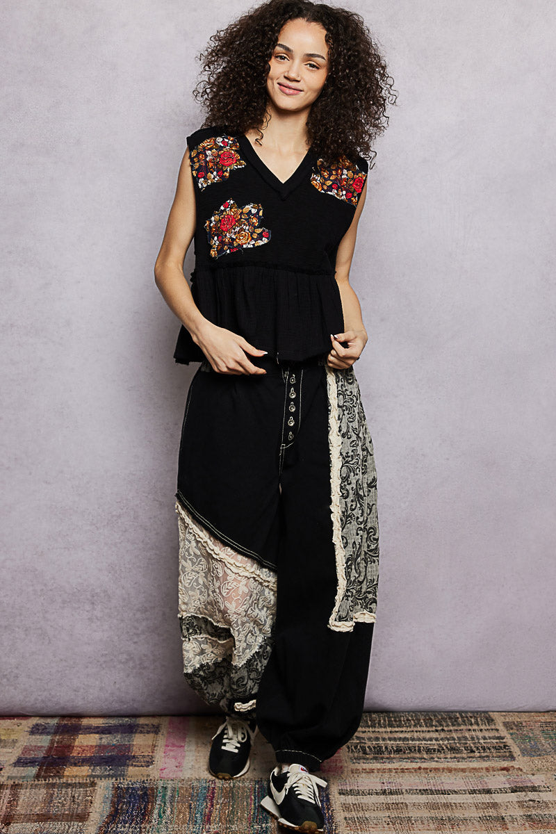 Woman wearing a black outfit with floral embroidery against a gray wall.