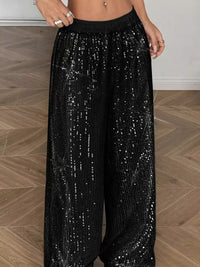 Black sequin pants worn by a person on a wooden floor.