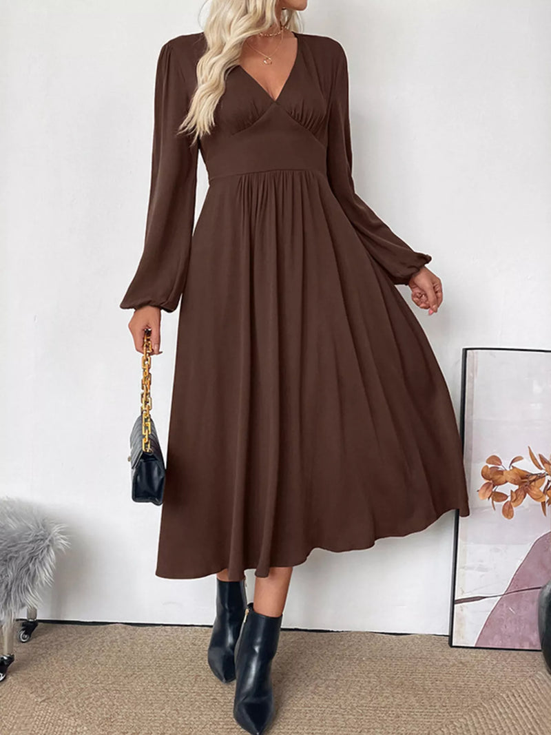 Woman wearing a brown dress with long sleeves against a white wall.