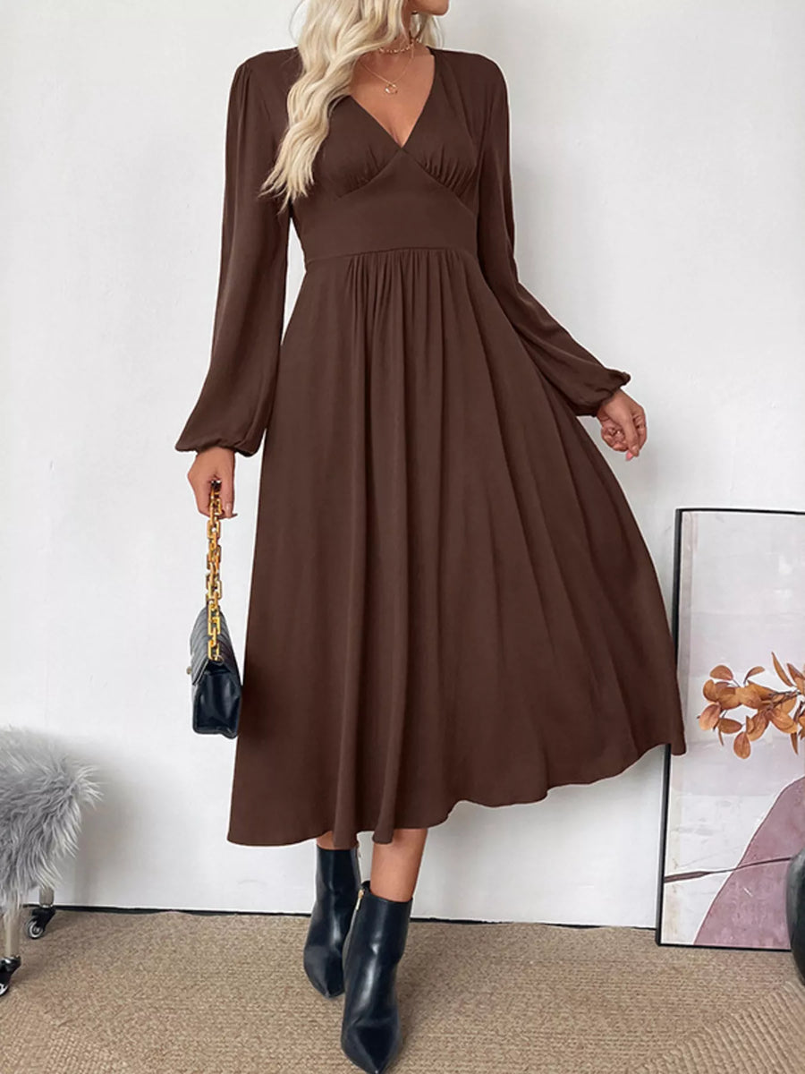 Woman wearing a brown dress with long sleeves against a white wall.