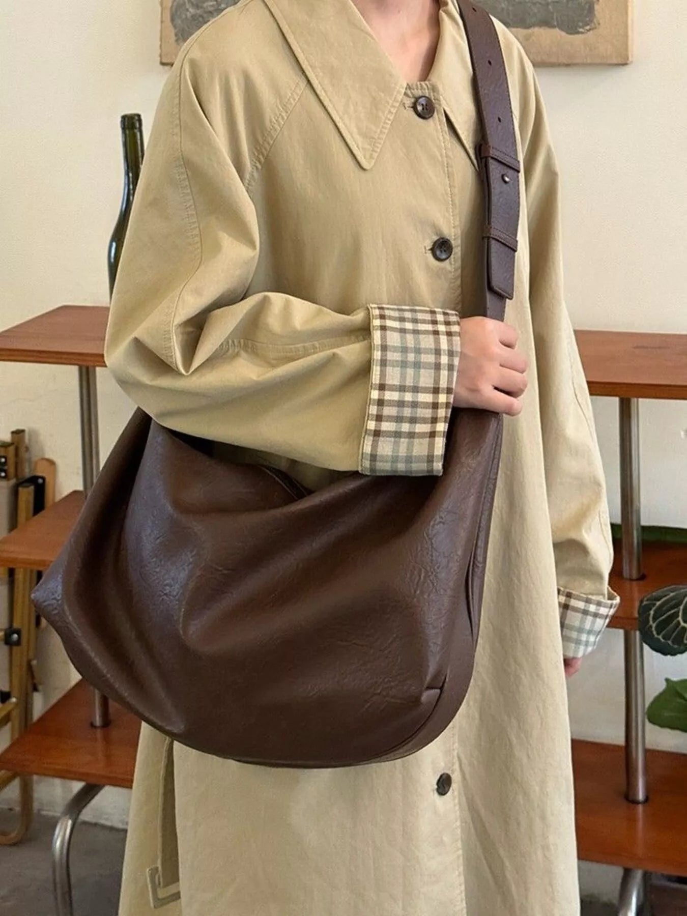 Person wearing a beige coat holding a brown leather bag indoors.