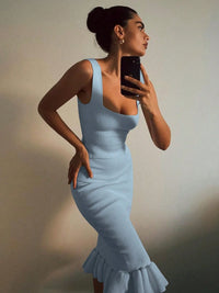 Woman in a light blue dress taking a mirror selfie against a neutral background