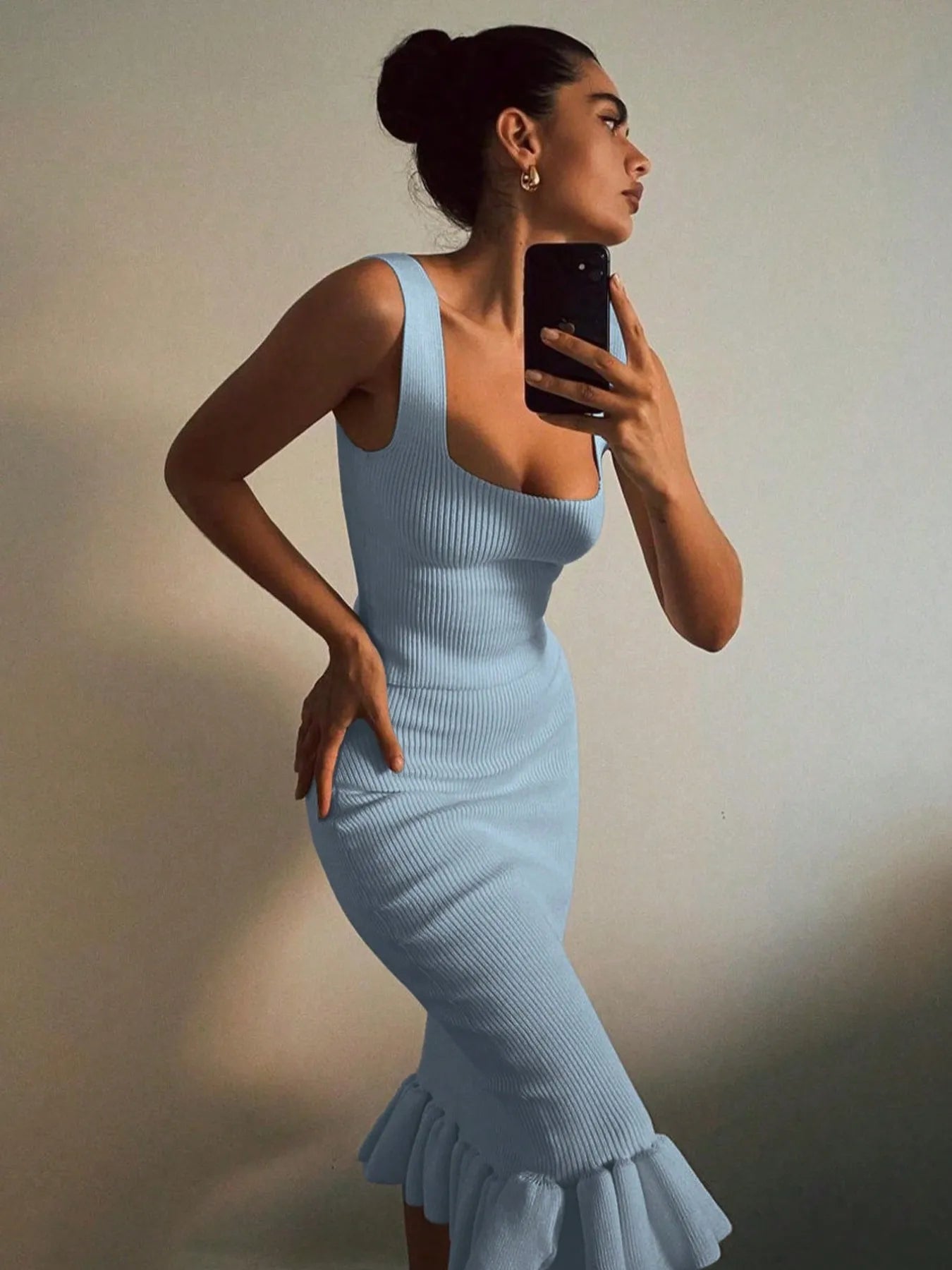 Woman in a light blue dress taking a mirror selfie against a neutral background