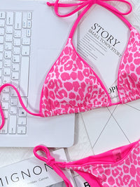 Pink leopard print bikini on a white surface with a laptop and magazine.