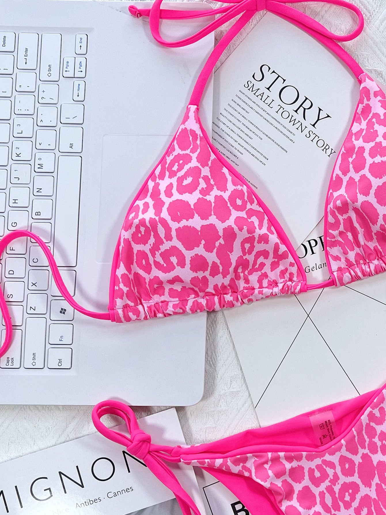 Pink leopard print bikini on a white surface with a laptop and magazine.