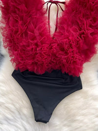 Red feathered top and black swimsuit on a white surface