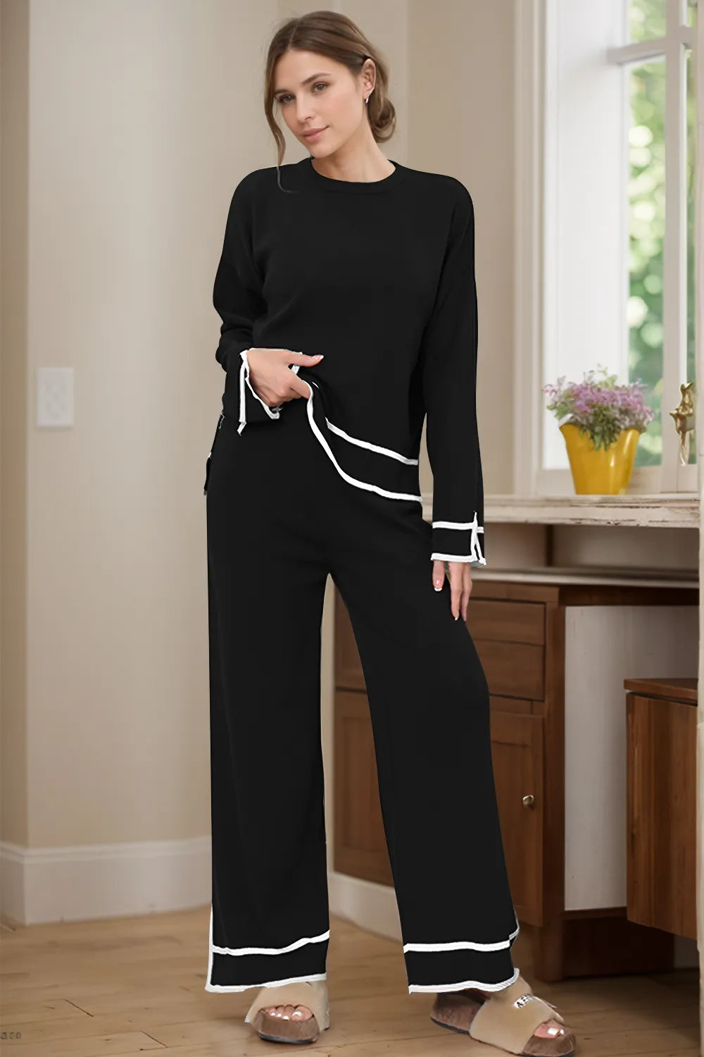 Woman wearing a black outfit with white trim in a room with wooden furniture and a window.
