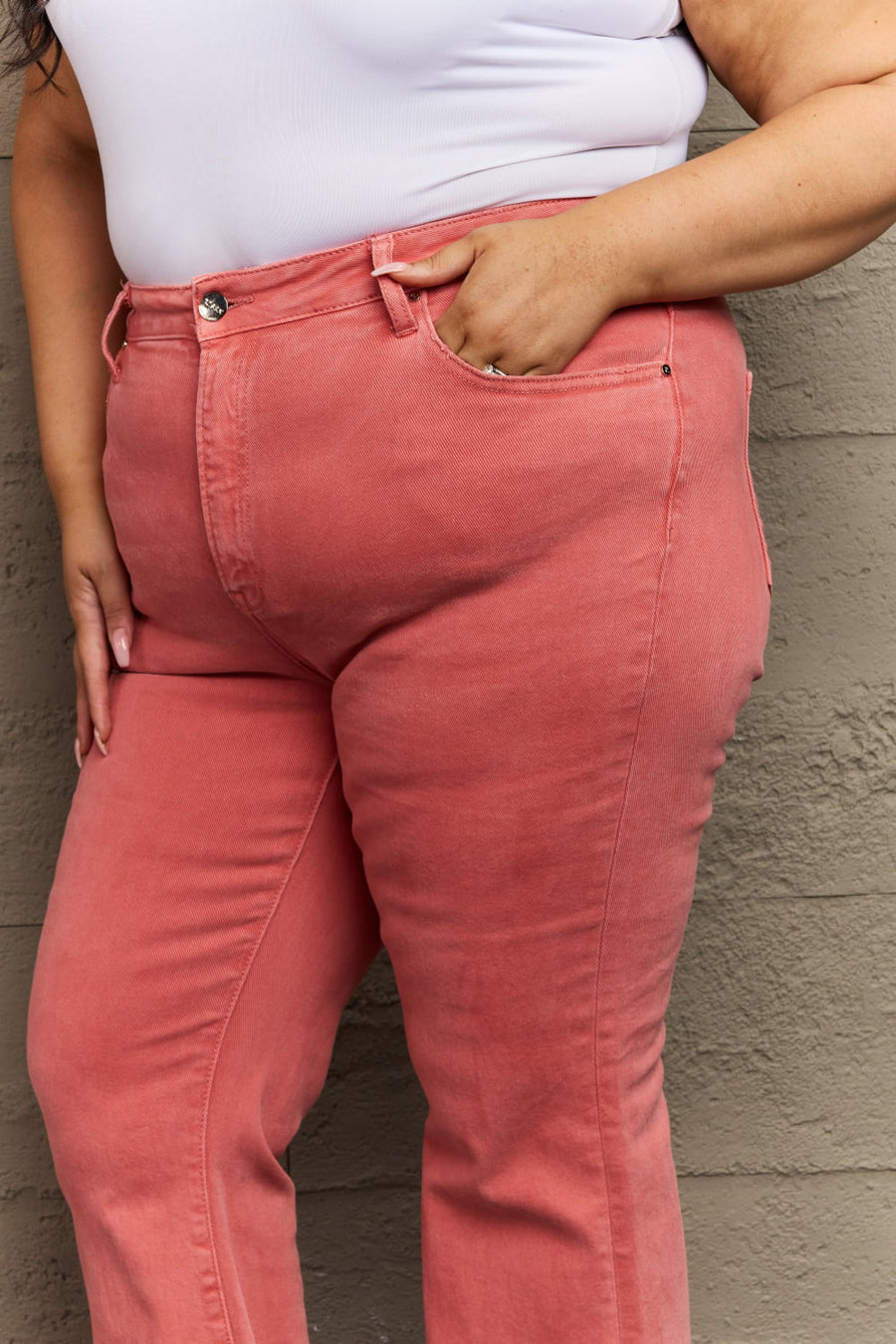 Person wearing pink pants with a white top against a textured wall.