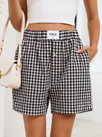 Person wearing black and white checkered shorts with a visible brand logo, holding a beige handbag.