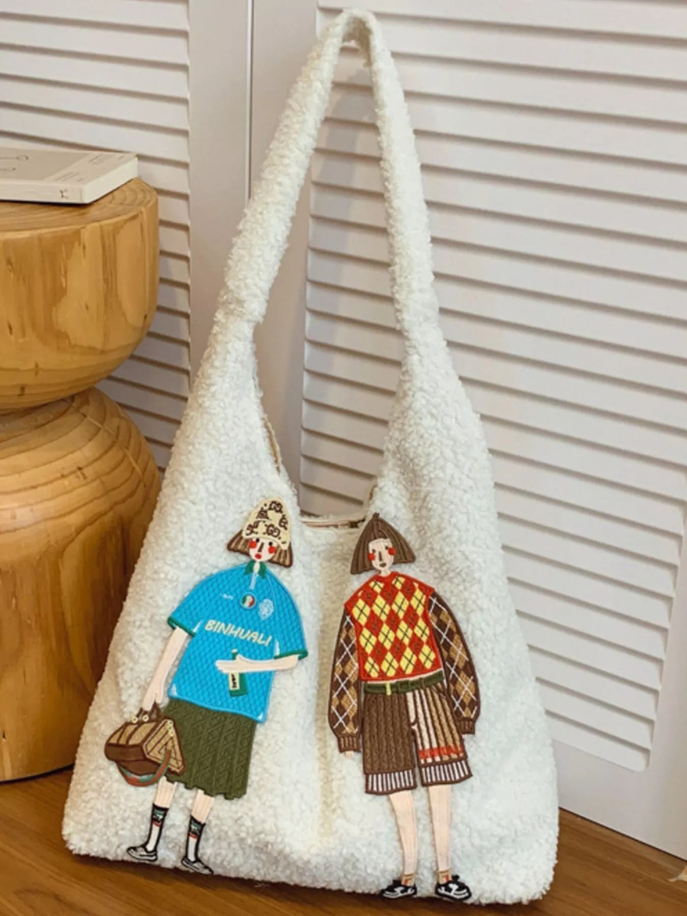 White textured bag with embroidered figures on a wooden surface