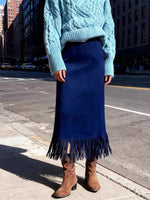 Person wearing a blue sweater, blue fringed skirt, and brown boots on a city street.