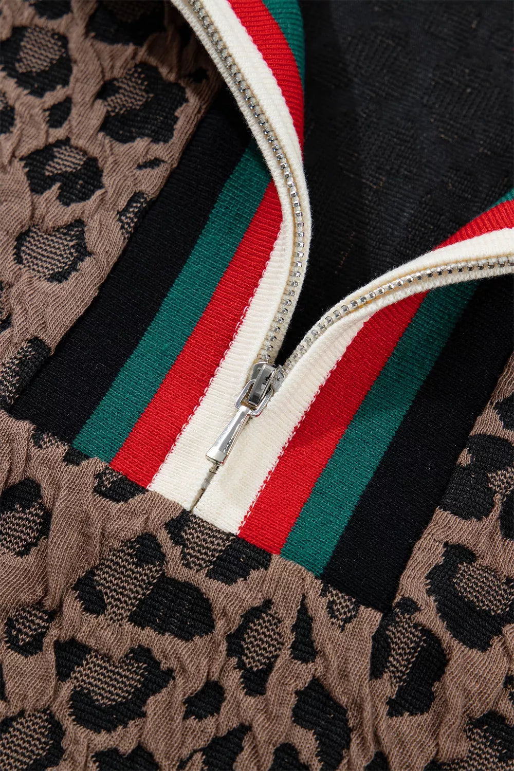 Close-up of a jacket with leopard print, red, green, and white zipper details.