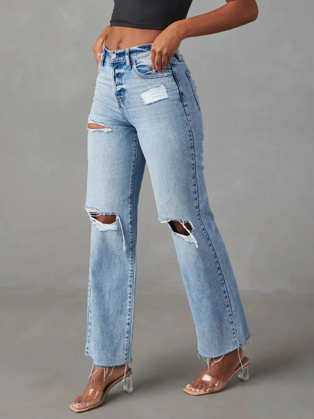 Person wearing light blue ripped jeans on a gray background