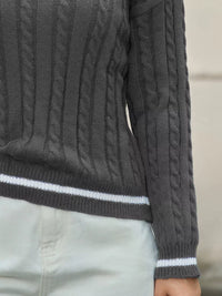 Dark gray cable knit sweater with white trim on a neutral background