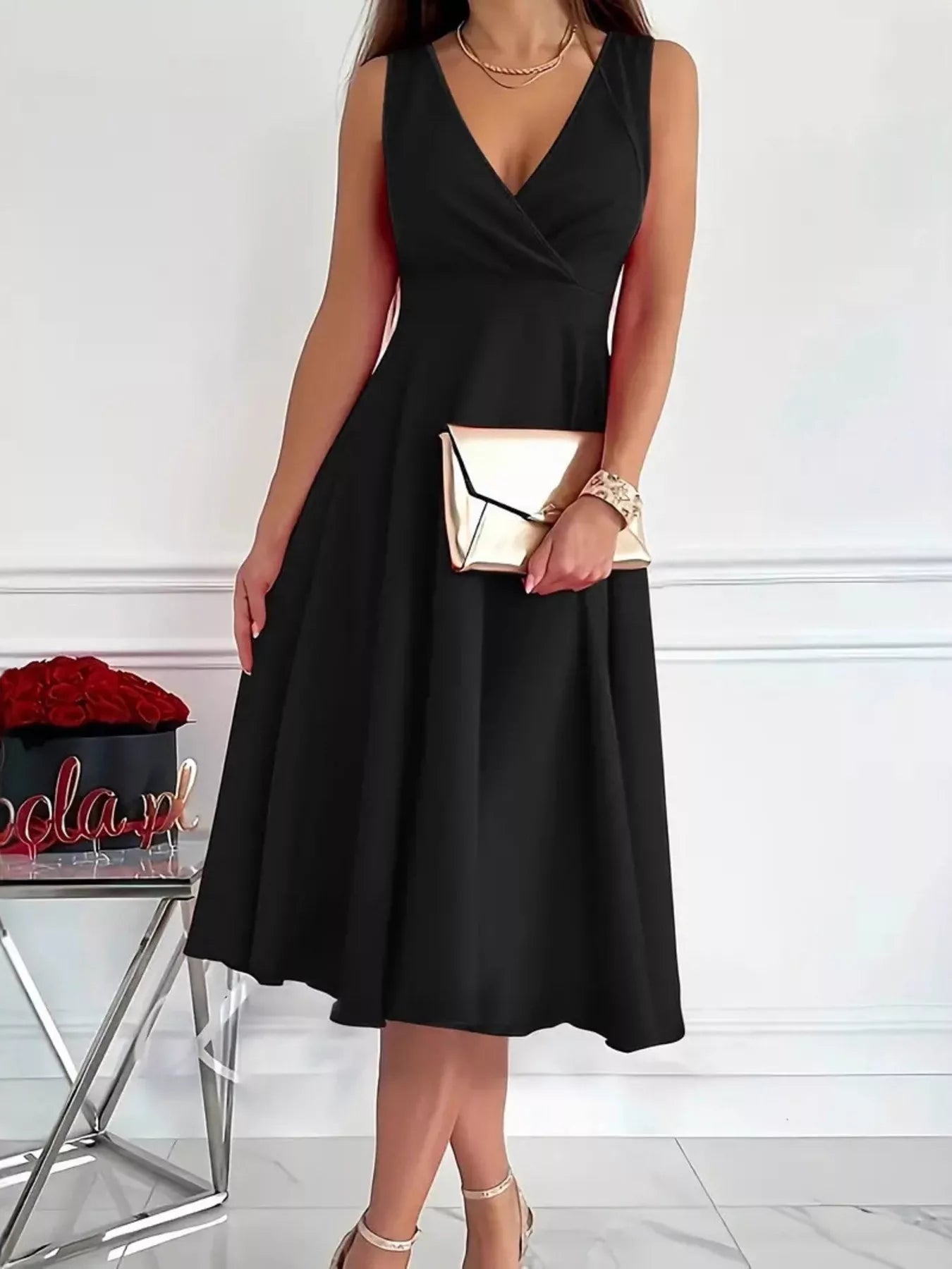 Woman wearing a black dress holding a gold clutch against a white background