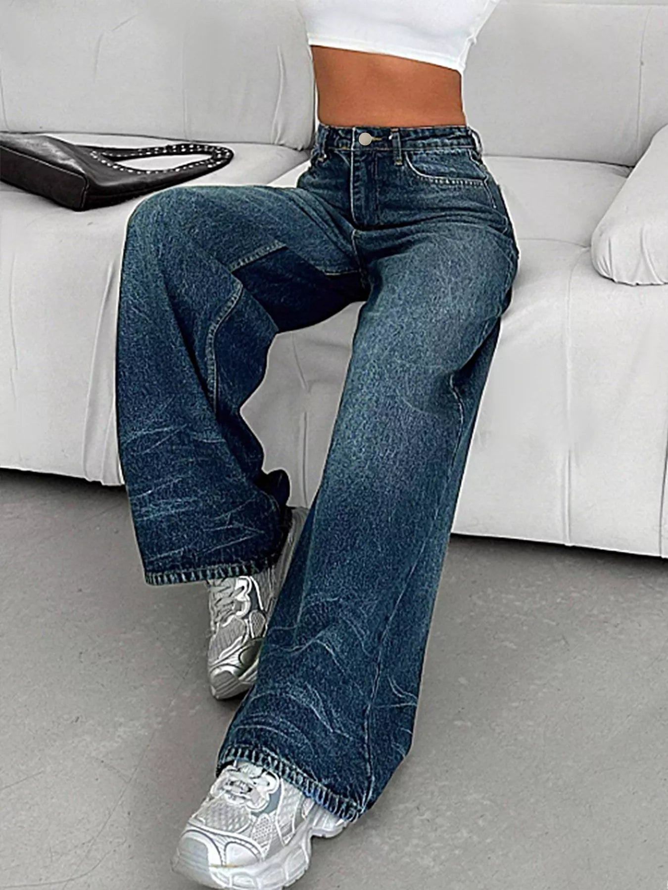 Person wearing blue jeans and white sneakers sitting on a white couch.